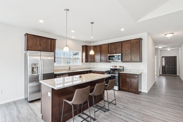 kitchen with appliances with stainless steel finishes, decorative light fixtures, a breakfast bar area, a center island, and light stone counters