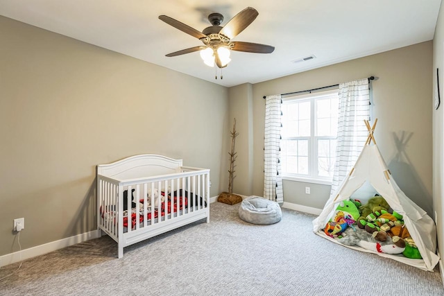 carpeted bedroom featuring a nursery area and ceiling fan