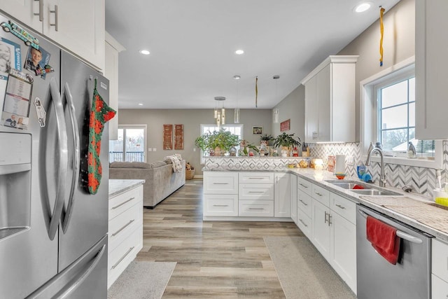 kitchen with appliances with stainless steel finishes, backsplash, sink, decorative light fixtures, and white cabinetry