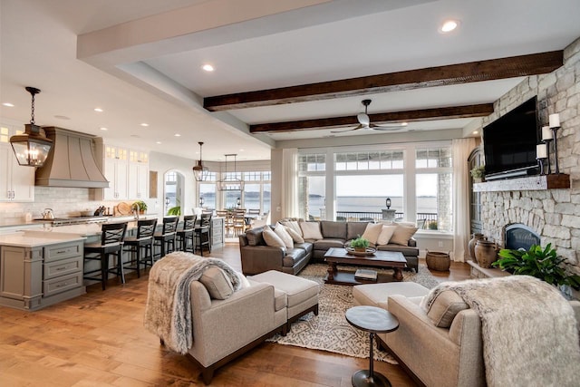 living room featuring a fireplace, light wood-type flooring, ceiling fan, and beamed ceiling