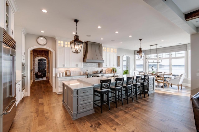 kitchen with custom exhaust hood, a large island with sink, pendant lighting, gray cabinets, and white cabinetry