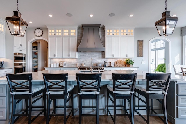 kitchen featuring custom range hood, white cabinetry, hanging light fixtures, and a spacious island