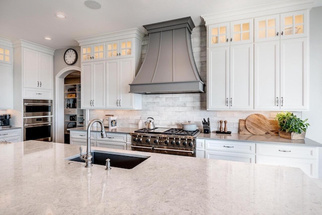 kitchen featuring light stone countertops, custom range hood, sink, and stainless steel appliances