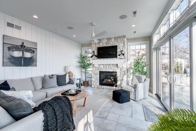 living room with ceiling fan, a fireplace, and wooden walls