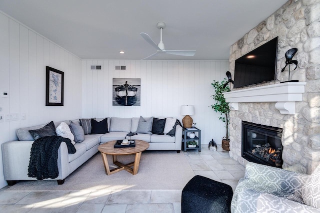 living room featuring a stone fireplace, ceiling fan, and wood walls