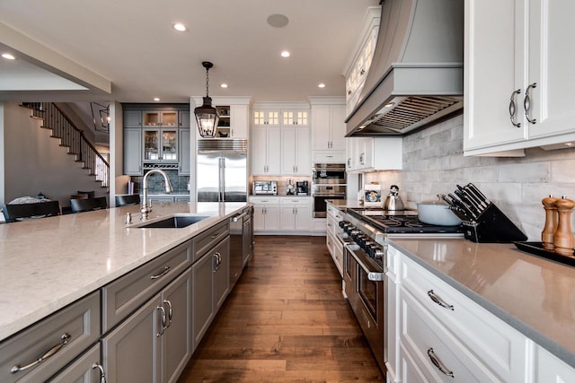 kitchen with sink, hanging light fixtures, premium range hood, white cabinets, and high end appliances