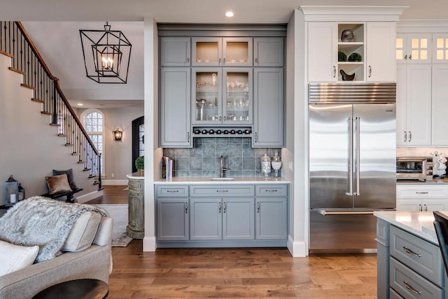 bar with stainless steel built in refrigerator, sink, hardwood / wood-style flooring, white cabinets, and hanging light fixtures