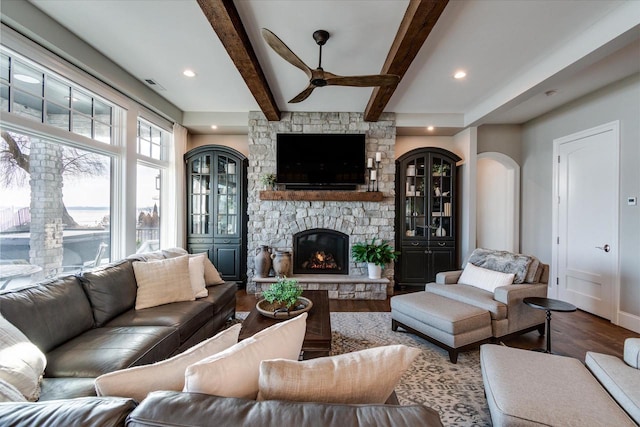 living room featuring beamed ceiling, wood-type flooring, a fireplace, and ceiling fan