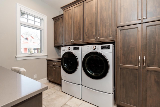 clothes washing area featuring washer and dryer, light tile patterned flooring, and cabinets