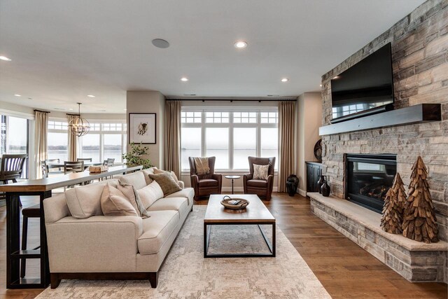 living room with hardwood / wood-style flooring, a stone fireplace, and an inviting chandelier