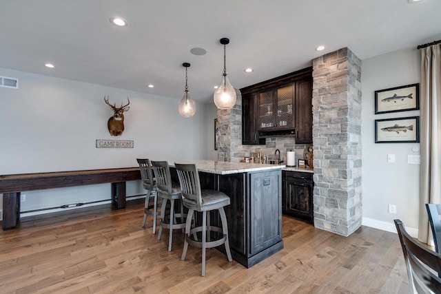 bar featuring light stone counters, light wood-type flooring, dark brown cabinetry, and hanging light fixtures