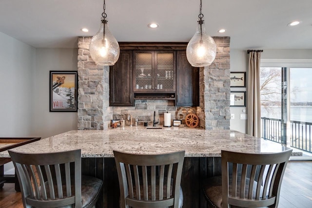 bar with decorative backsplash, hardwood / wood-style floors, dark brown cabinetry, and decorative light fixtures