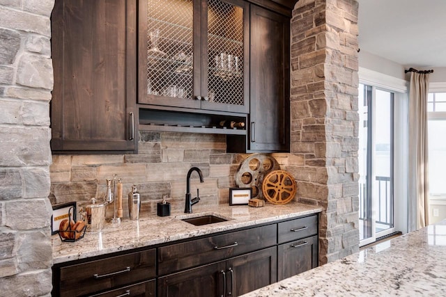 kitchen featuring dark brown cabinetry, backsplash, light stone counters, and sink