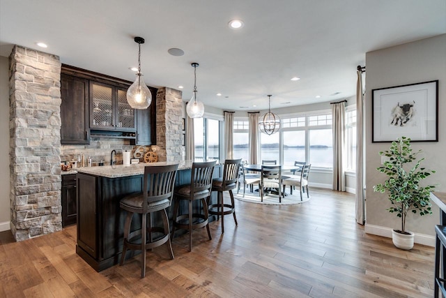 bar with light stone countertops, light wood-type flooring, dark brown cabinetry, and a water view