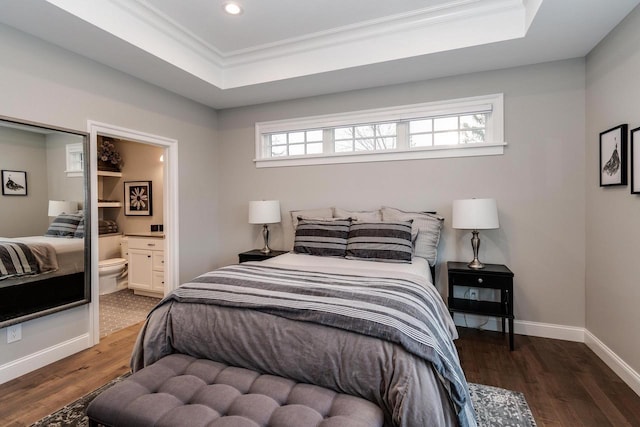 bedroom featuring dark wood-type flooring, ornamental molding, ensuite bathroom, and a tray ceiling