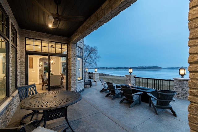 patio terrace at dusk featuring ceiling fan, a water view, and an outdoor fire pit