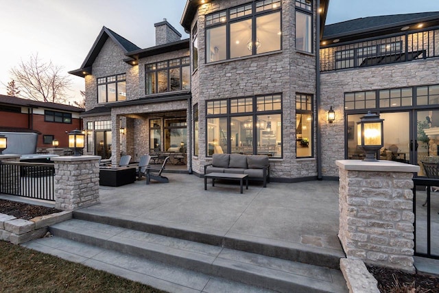 back house at dusk featuring a patio and an outdoor living space with a fire pit