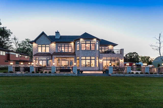 back house at dusk featuring a lawn and a balcony