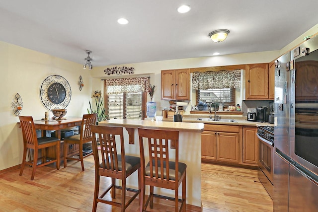 kitchen with a breakfast bar area, sink, light hardwood / wood-style floors, and appliances with stainless steel finishes