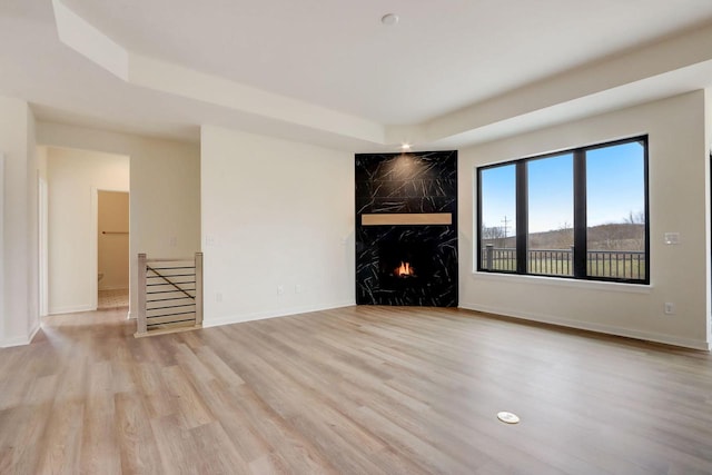 unfurnished living room featuring a high end fireplace, a tray ceiling, and light wood-type flooring