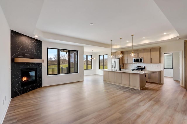 kitchen featuring sink, appliances with stainless steel finishes, an island with sink, decorative light fixtures, and a raised ceiling