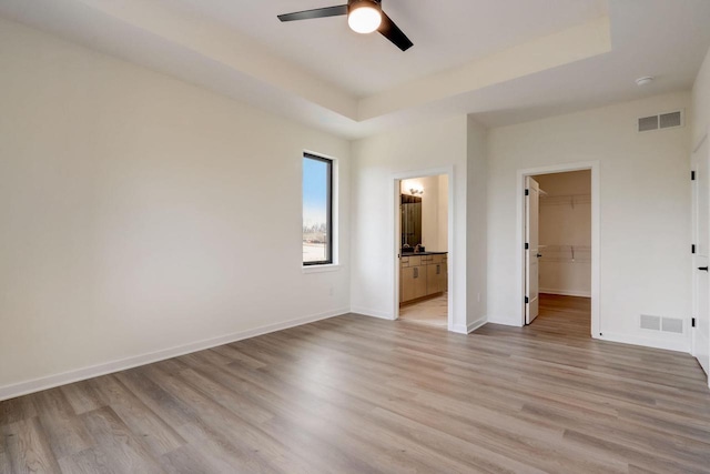 unfurnished bedroom featuring a walk in closet, a tray ceiling, and light hardwood / wood-style floors