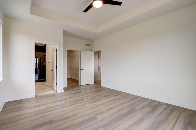 unfurnished bedroom featuring a tray ceiling, light hardwood / wood-style flooring, and a spacious closet