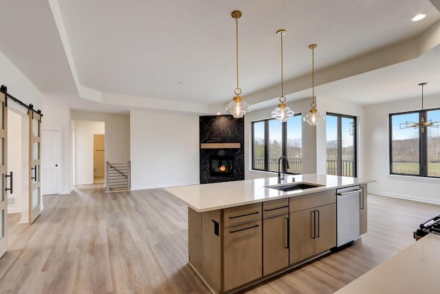 kitchen featuring sink, dishwasher, a kitchen island with sink, decorative light fixtures, and a barn door