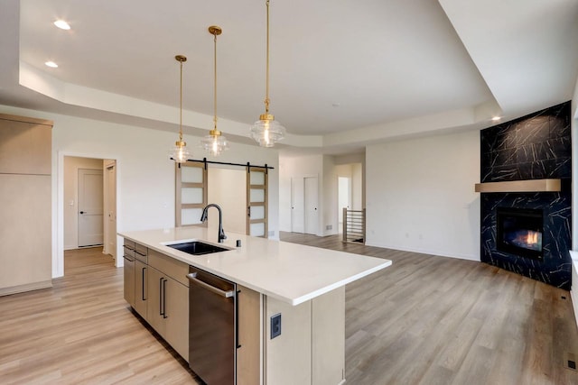 kitchen with a tray ceiling, a barn door, sink, and a center island with sink