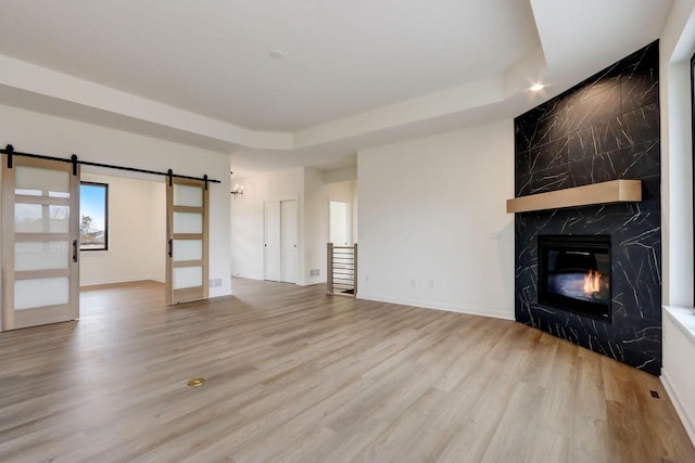 unfurnished living room featuring a fireplace, a barn door, a raised ceiling, and light wood-type flooring