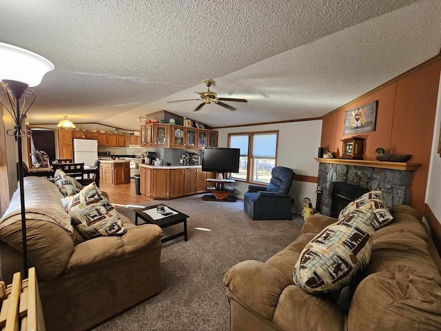 carpeted living room with vaulted ceiling, a stone fireplace, and ceiling fan