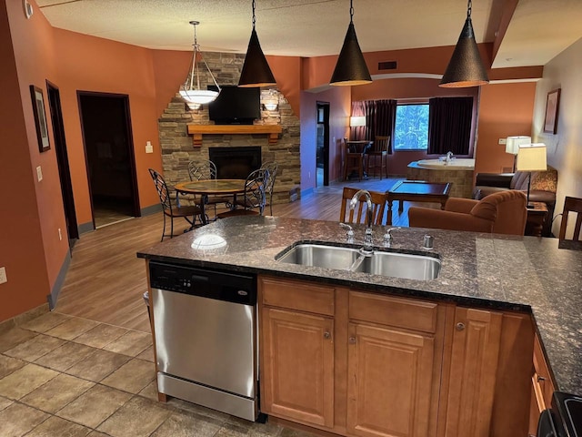 kitchen with dishwasher, sink, dark stone countertops, decorative light fixtures, and a fireplace