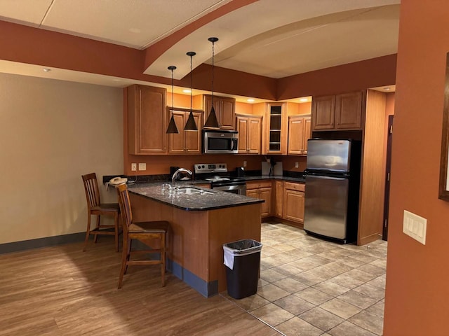 kitchen with pendant lighting, dark stone counters, sink, kitchen peninsula, and stainless steel appliances