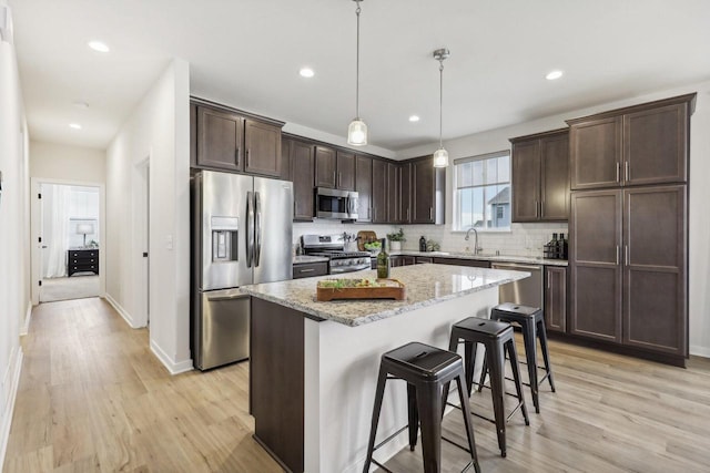 kitchen featuring pendant lighting, a center island, a kitchen breakfast bar, appliances with stainless steel finishes, and light stone counters