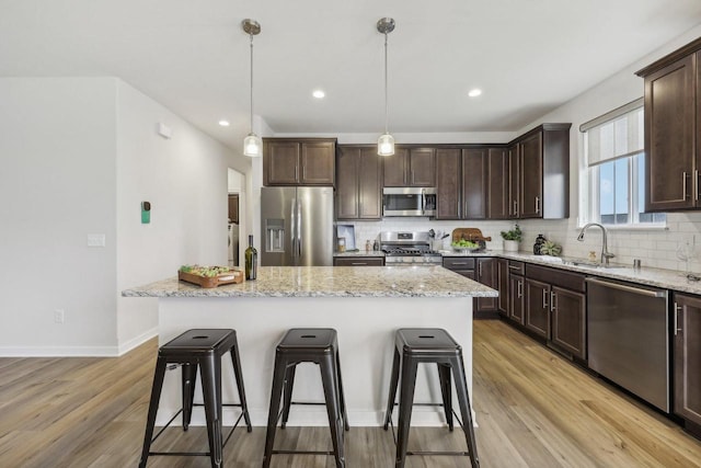 kitchen with light stone countertops, appliances with stainless steel finishes, light hardwood / wood-style flooring, a center island, and hanging light fixtures