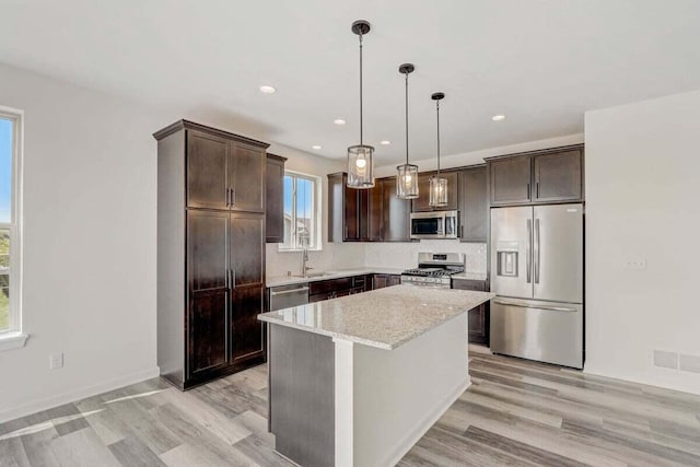 kitchen featuring light stone counters, stainless steel appliances, decorative light fixtures, light hardwood / wood-style flooring, and a kitchen island