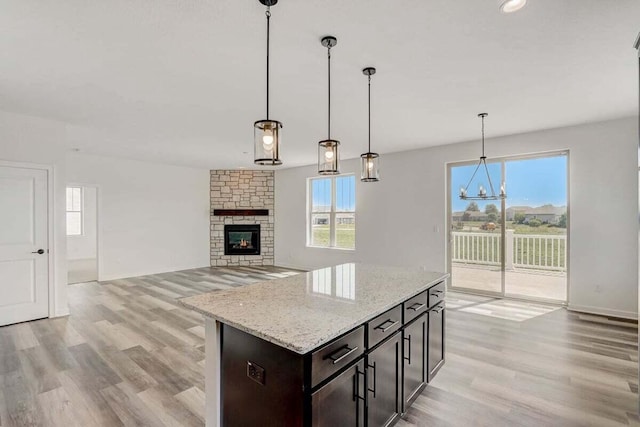 kitchen with a stone fireplace, light stone counters, dark brown cabinets, and decorative light fixtures