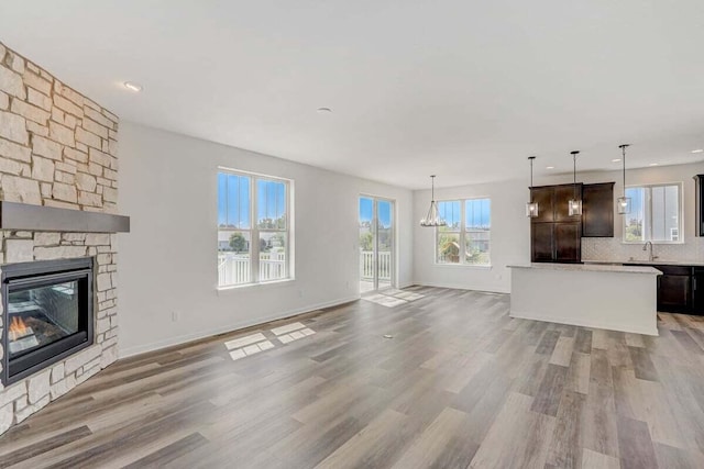 unfurnished living room featuring sink, a fireplace, light hardwood / wood-style floors, and a notable chandelier