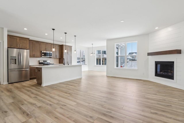 kitchen featuring hanging light fixtures, an island with sink, stainless steel appliances, light hardwood / wood-style floors, and backsplash