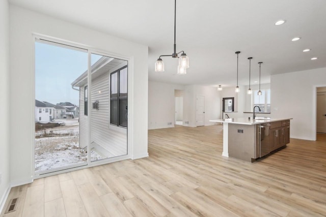 kitchen with pendant lighting, sink, light hardwood / wood-style flooring, dishwasher, and a kitchen island with sink