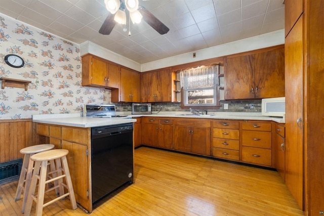 kitchen featuring a kitchen bar, ceiling fan, sink, light hardwood / wood-style flooring, and black dishwasher