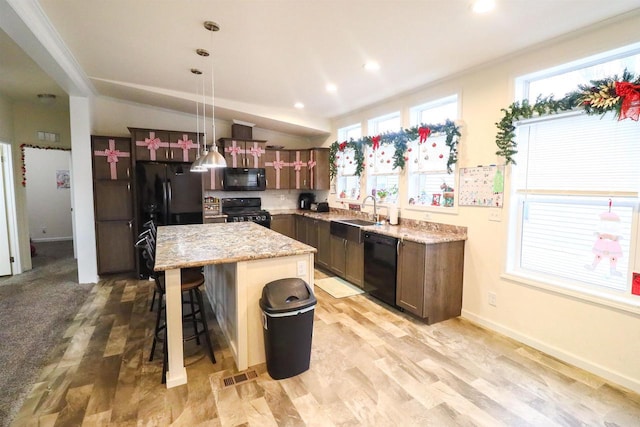 kitchen featuring sink, hanging light fixtures, light stone counters, a kitchen island, and black appliances