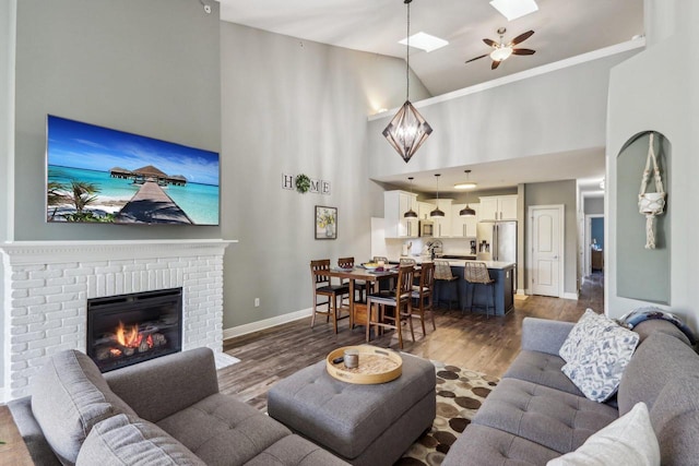 living room featuring sink, a brick fireplace, dark hardwood / wood-style flooring, high vaulted ceiling, and ceiling fan with notable chandelier