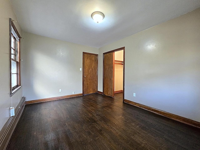 empty room with baseboard heating and dark hardwood / wood-style floors