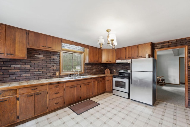 kitchen with stainless steel appliances, sink, pendant lighting, tile countertops, and a chandelier