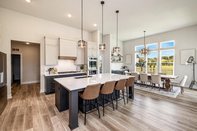 kitchen featuring a kitchen bar, a kitchen island with sink, light hardwood / wood-style flooring, and decorative light fixtures