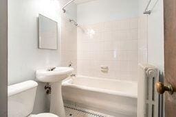 bathroom featuring radiator heating unit, tiled shower / bath combo, and toilet