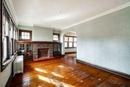 unfurnished living room with radiator heating unit, crown molding, dark wood-type flooring, and a brick fireplace