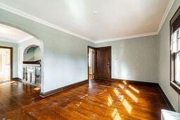 empty room featuring dark wood-type flooring, a wealth of natural light, and crown molding