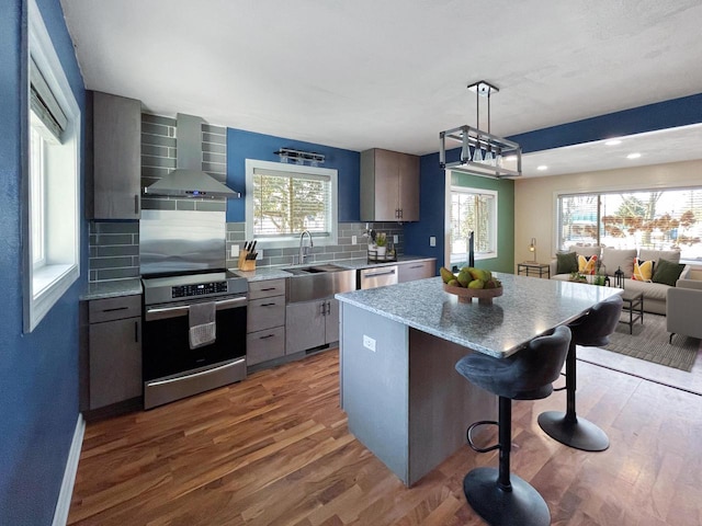 kitchen featuring wall chimney range hood, dark hardwood / wood-style flooring, decorative backsplash, a kitchen island, and appliances with stainless steel finishes